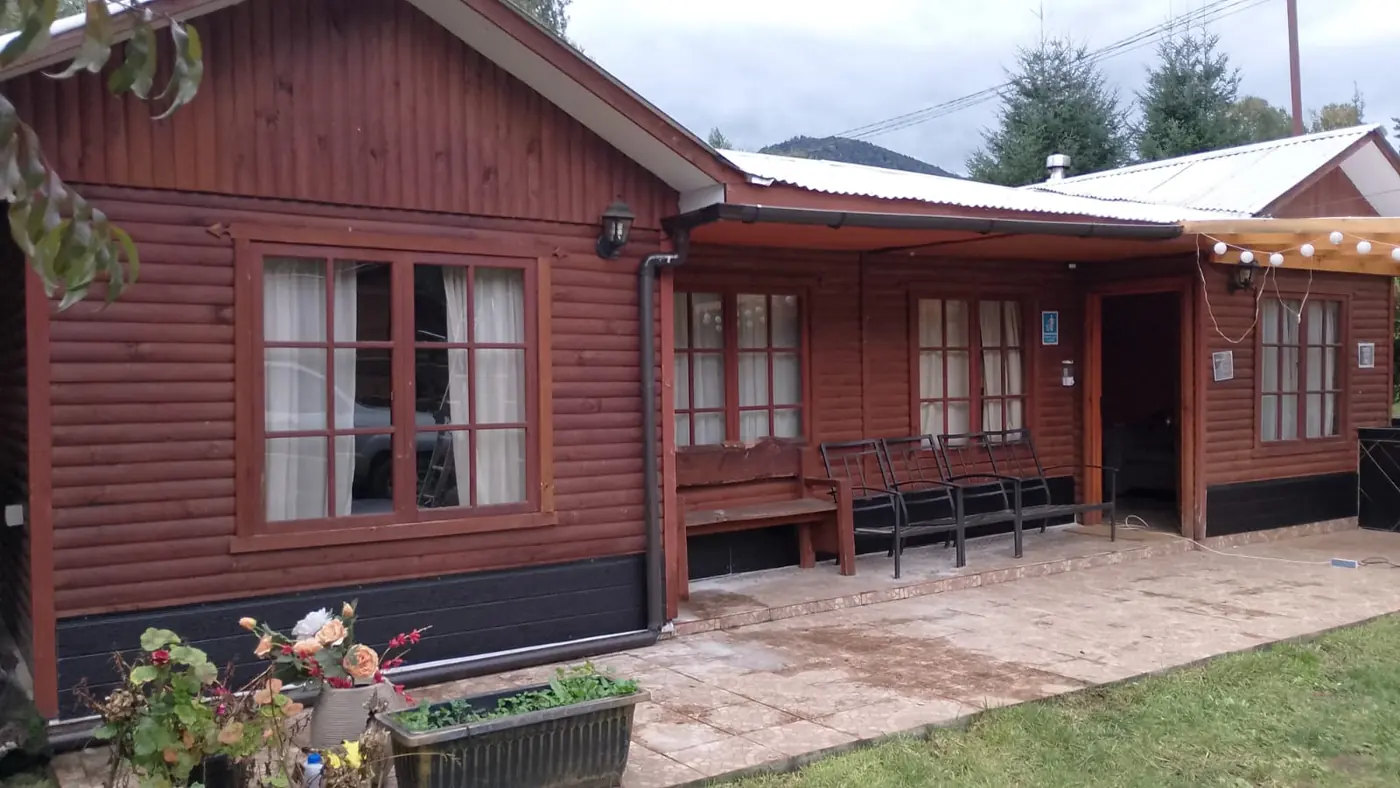 La cabaña de madera por fuera, con la terraza, el quincho y el jardín