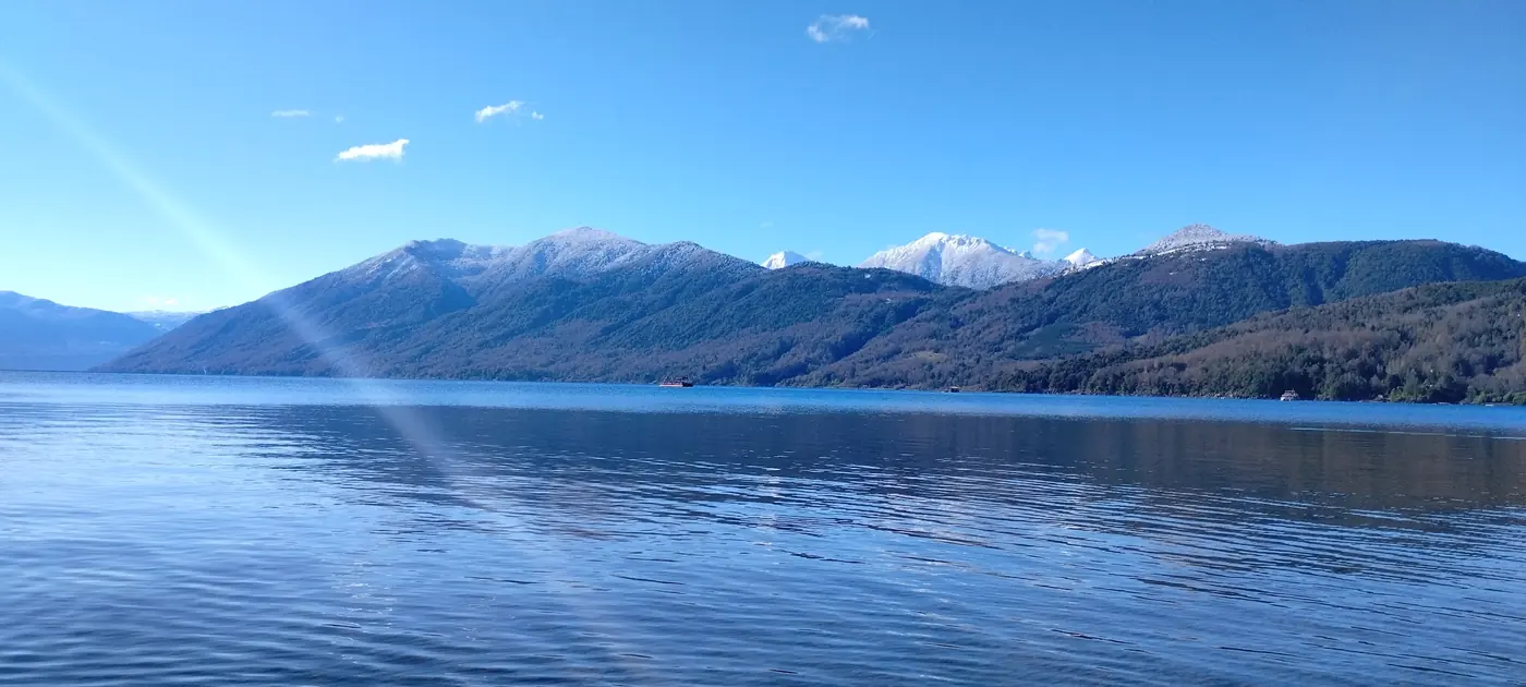 El lago con el sol entre las nubes y las montañas nevadas